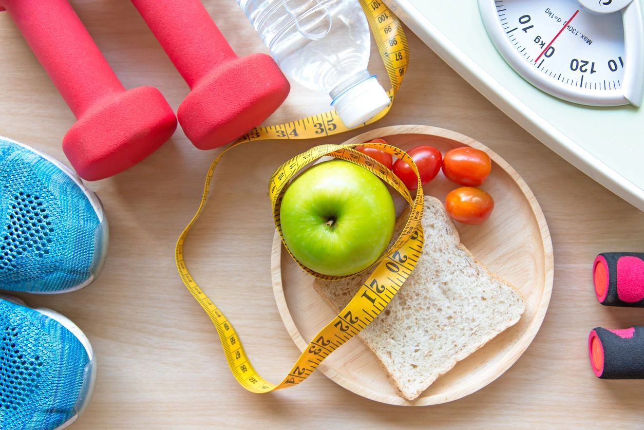 sneakers, dumbbells, a healthy snack, a scale and a measuring tape indicative of a New Year's resolution