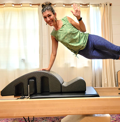 Tanya waving hello from atop Pilates reformer at Flow in Asheville